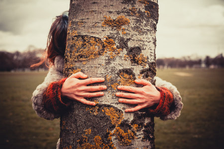 Young woman is in the park on a winter's day and is hugging a treeの写真素材