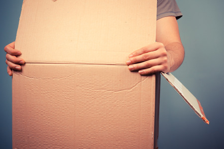 Young man is moving house and is holding a large cardboard boxの写真素材