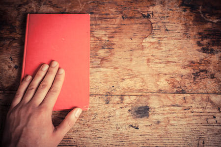 A man is resting his left hand on a red book at a tableの写真素材