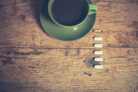 A cup of black coffee with six pills next to itの写真素材