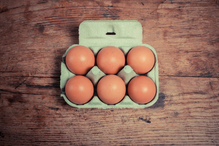 Six eggs in a cardboard tray on a wooden table