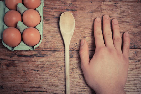 Man resting his hand next to eggs and a wooden spoon on a tableの写真素材