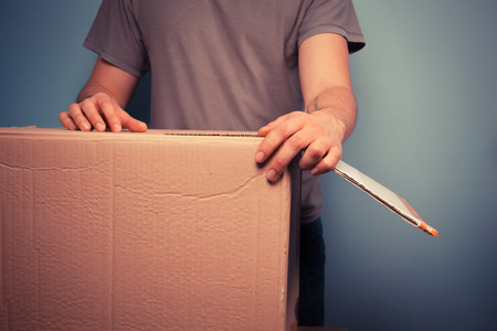 Young man is moving house and is holding a large cardboard boxの写真素材