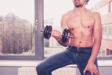 Young athletic shirtless man is working out by the windowの写真素材