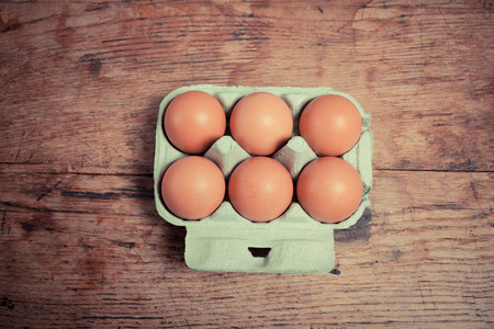 Six eggs in a cardboard tray on a wooden tableの写真素材