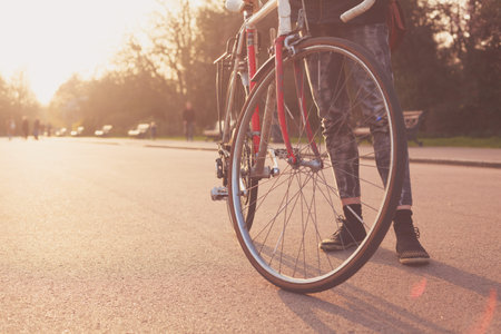 A Young woman is standing with her bicycle in the park at sunset