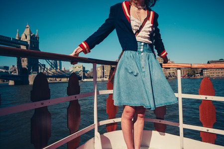A young woman's skirt is blowing in the wind as she is standing on the deck of a boat cruising down the riverの写真素材
