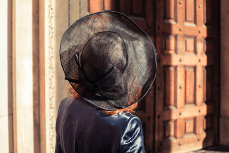 Young woman wearing a hat is walking and looking at an old buildingの写真素材