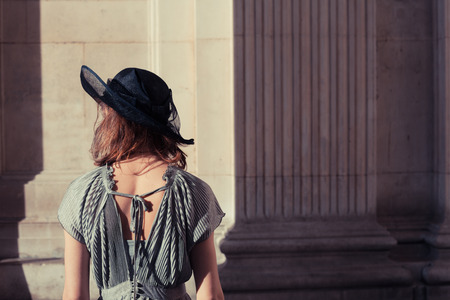 Young woman wearing an elegant dress and hat is standing in an impressive and majestic hall bathed in sunlightの写真素材