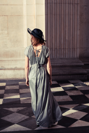 Young woman wearing an elegant dress and hat is standing in an impressive and majestic hall bathed in sunlightの写真素材