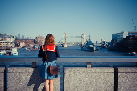 A young woman is standing on London bridge and admiring the skyline and the river Thamesの写真素材