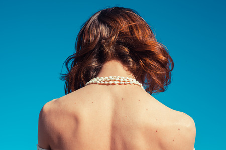 A young woman is tanning her back on a sunny day with a clear blue skyの写真素材