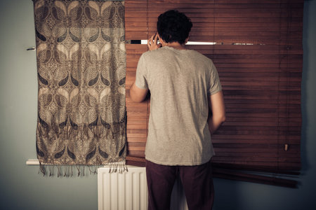 A peeping tom is looking out through his blinds and is masturbating