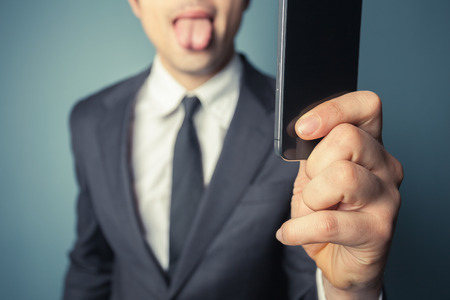 Young businessman is taking a selfie with his smart phone and sticking his tongue outの写真素材