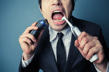 A stressed businessman is late and is shaving and brushing his teeth at the same timeの写真素材