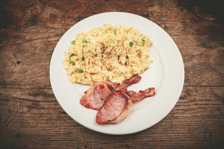 Bacon and scrambled eggs on a white plateの写真素材