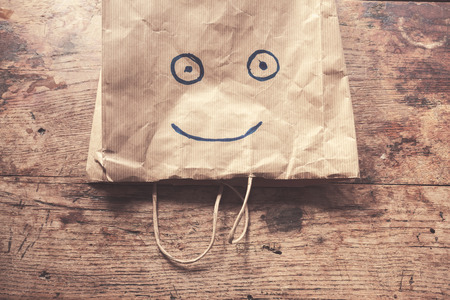 A paperbag with a smiling face painted on it lying on a wood tableの写真素材