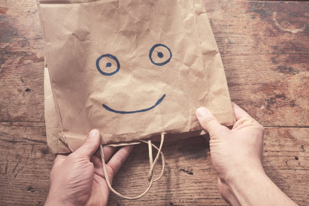 Man holding a paperbag with a smiling face painted on it