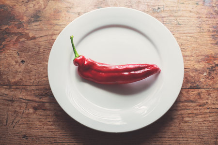 Large red pepper and a plate on a wood table in the sunlightの写真素材