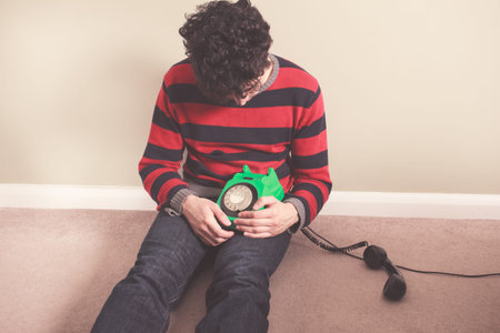 Sad man sitting on the floor has received bad news on the telephone