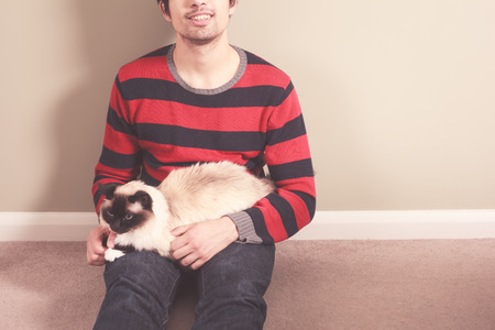 A young man is sitting on the floor and petting his catの写真素材