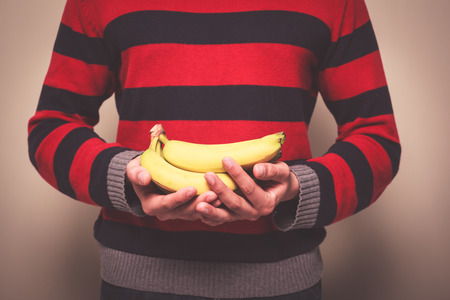Closeup on a man in a striped jumper holding a bunch of bananasの写真素材