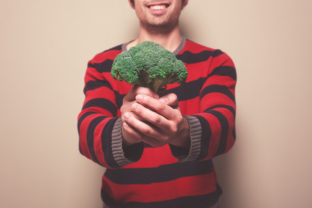 A young man is holding a floret of broccoliの写真素材