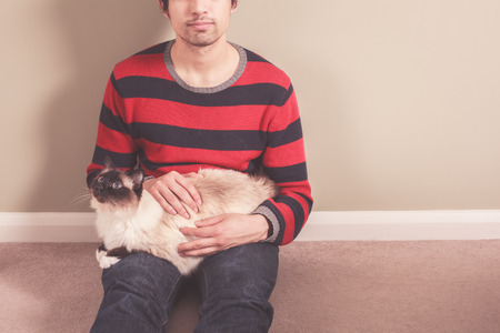 A young man is sitting on the floor and petting his catの写真素材