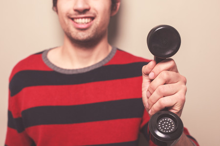 A happy young man is holding a telephone receiverの写真素材