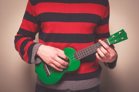 Young man in a striped jumper is playing ukulele