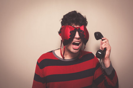 Young man wearing a bra on his face is answering the telephone