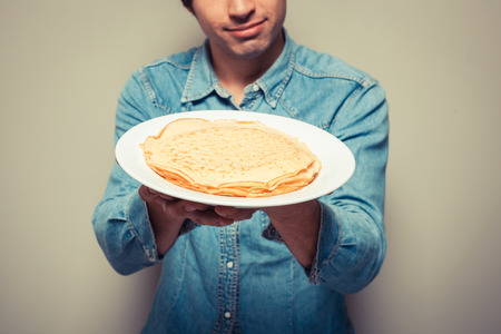 Young man is presenting a plate with a stack of pancakesの写真素材