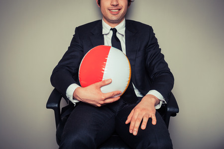 A businessman is sitting in an office chair with a beach ballの写真素材
