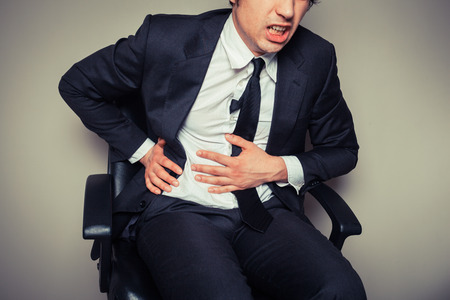 A young businessman sitting in an office chair is having stomach painsの写真素材
