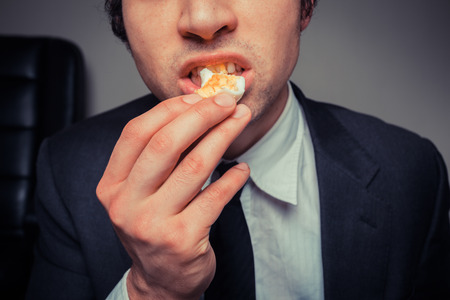 A businessman sitting in an office chair is eating an eggの写真素材