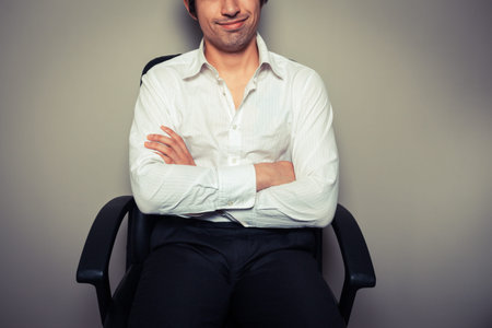 A casual and happy young businessman is sitting in an office chair