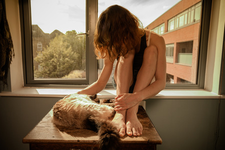 Young woman relaxing with her cat by the windowの写真素材