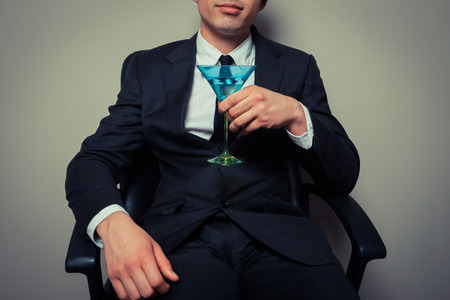 Young businessman sitting in an office chair with a cocktailの写真素材