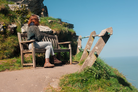 Young woman is sitting on a bench on top of a cliffの写真素材