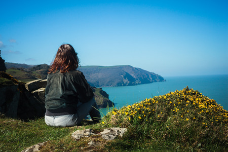 Young woman is sitting on the edge of a cliff by the seaの写真素材