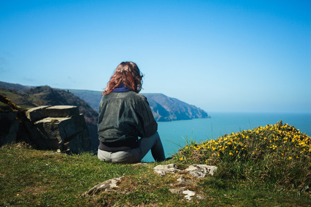 Young woman is sitting on the edge of a cliff by the seaの写真素材
