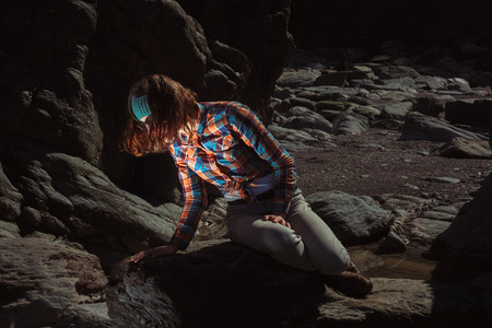 Young woman is sitting on a rock and looking at something excitingの写真素材