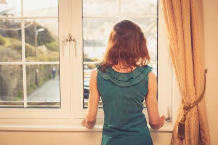 Young woman wearing an elegant dress is looking out the windowの写真素材