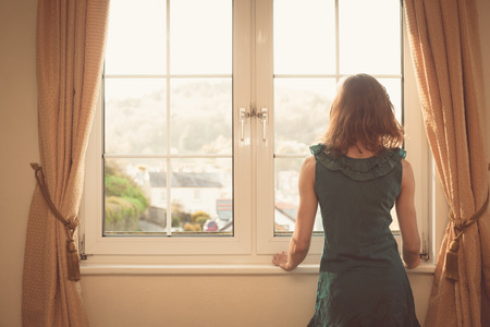 Young woman wearing an elegant dress is looking out the windowの写真素材