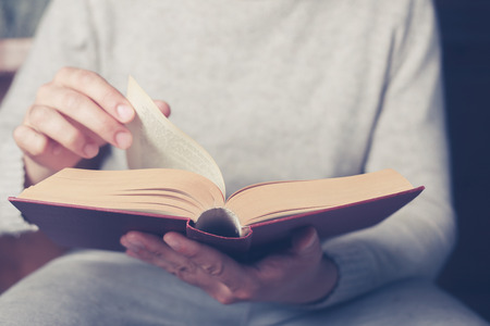Young man is sitting on a sofa and flipping the pages of a big bookの写真素材