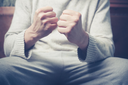 Young man is sitting on a sofa with his fists clenchedの写真素材