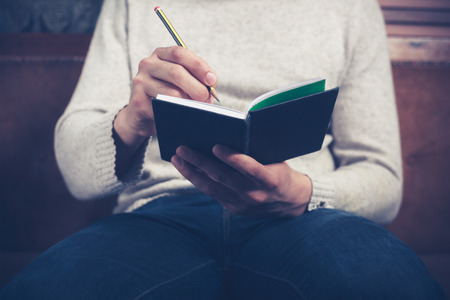 A man is sitting on a sofa and writing notes in a notebookの写真素材