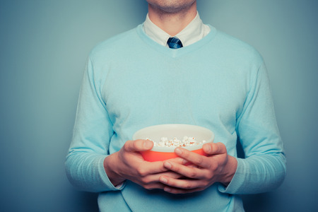 A young man is holding a bowl of popcornの写真素材