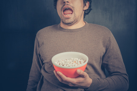 A shocked young man is holding a bowl of popcornの写真素材
