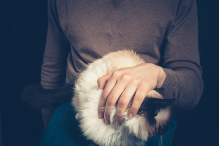Young man is sitting with a cat on his lapの写真素材